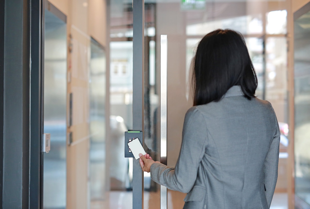 Young officer woman holding a key card to lock and unlock door for access entry. Door access control. Back view.